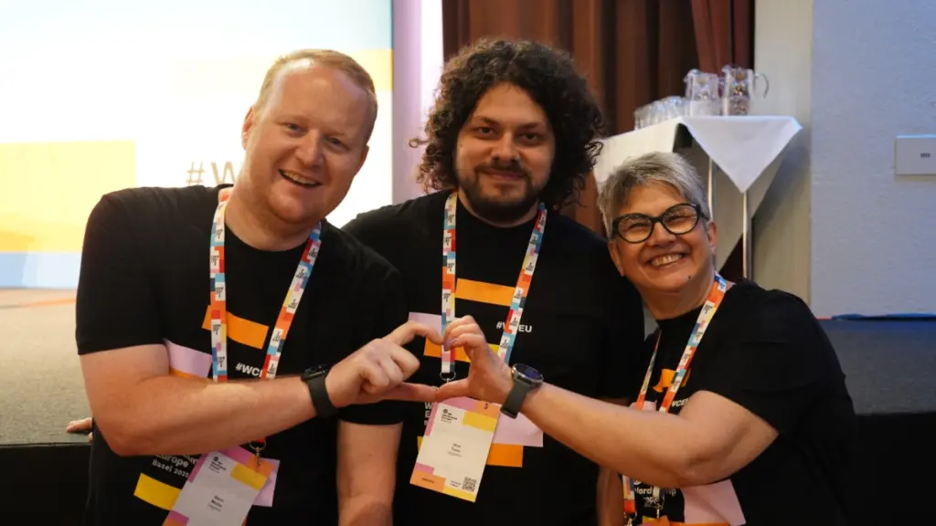 WordCamp Europe 2025 lead organisers, Steve, Uroš and Laura, creating a heart with their hands. Photo by Nilo Velez